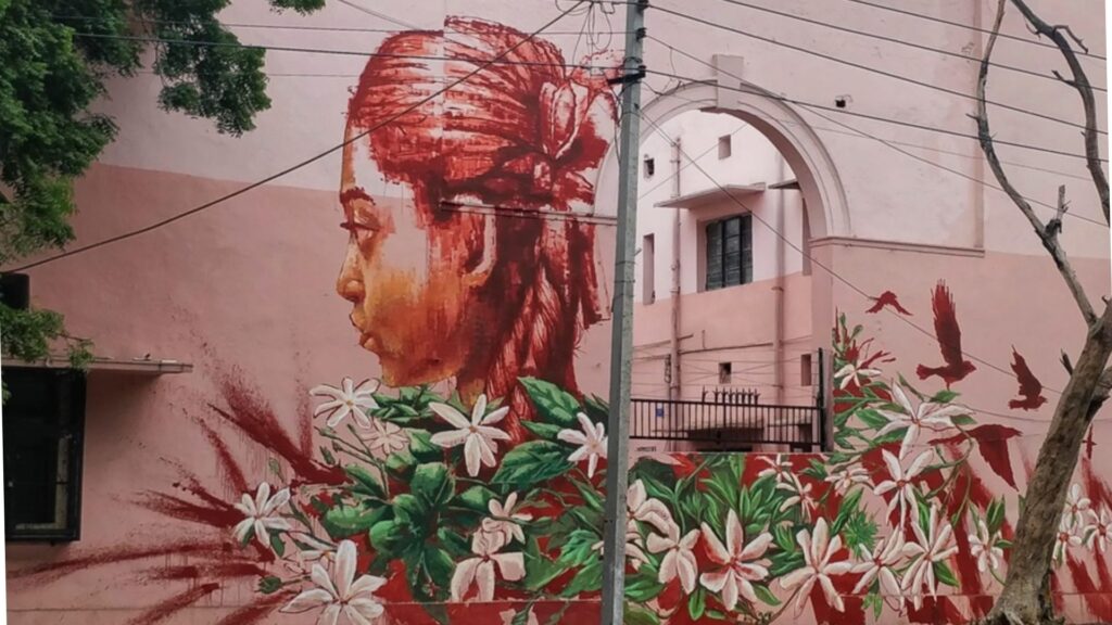 Painted mural of girl with flowers on pink wall in Lodhi Art District, one of the best off the beaten path sites in Delhi