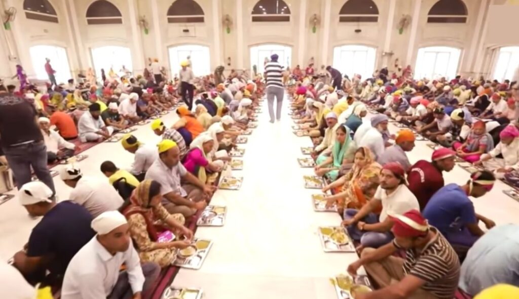 Gurudwara Bangla Sahib langar hall, Delhi with rows of devotees sitting on the floor eating from metal trays