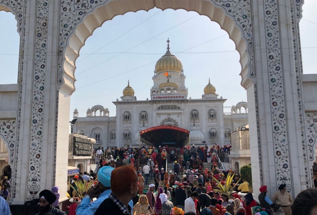 White arched entrance to the Bangla Sahib complex with view of temple through the arch and crowds of people
