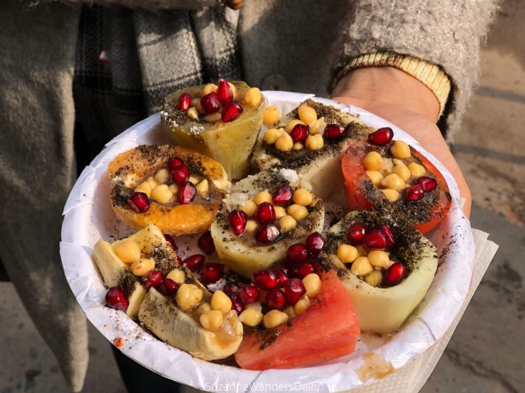 a white paper palte of fruit chaat in Old Delhi being held by hand at Hira Laal Chaat Corner in Old Delhi, a must on every street food tour