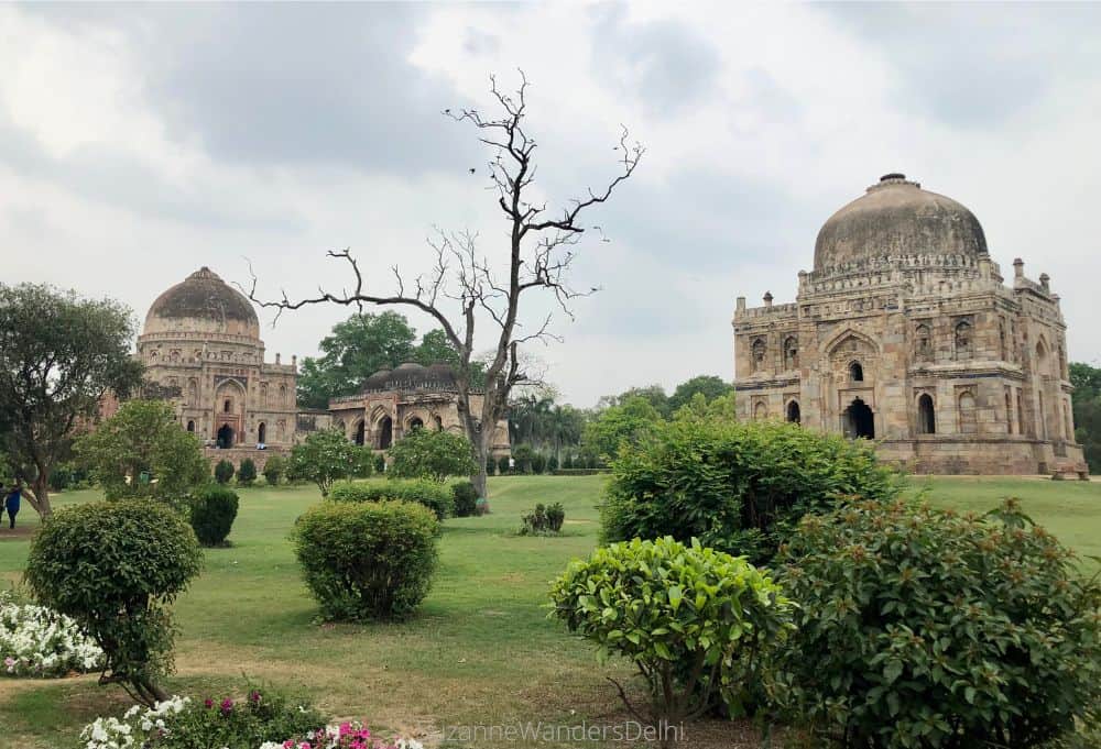 Two mughal tombs and a mosque in a park with green grass and shrubbery