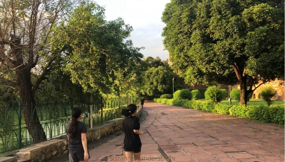 two joggers on a wide paved path with trees and a water reservoir on each side / Where to Go in Delhi With Your Dog - The Ultimate Guide