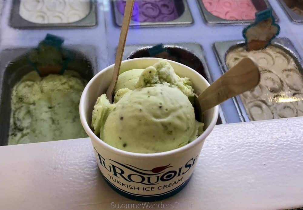 a cup of pistachio ice cream with 2 wooden spoons and the ice cream freezer/display in background.  This is the best Turkish ice cream in Delhi.