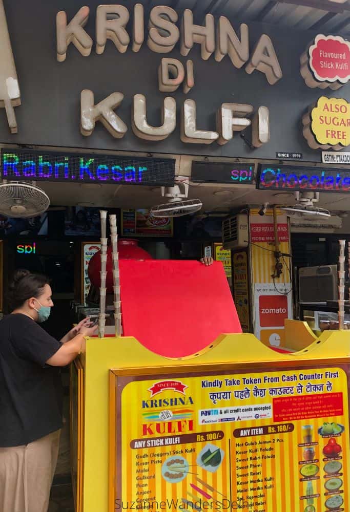 The yellow outdoor cart with big Krishna di Kulfi signage behind and person ordering kulfi - the location alone makes this one one of the best places in Delhi for ice cream