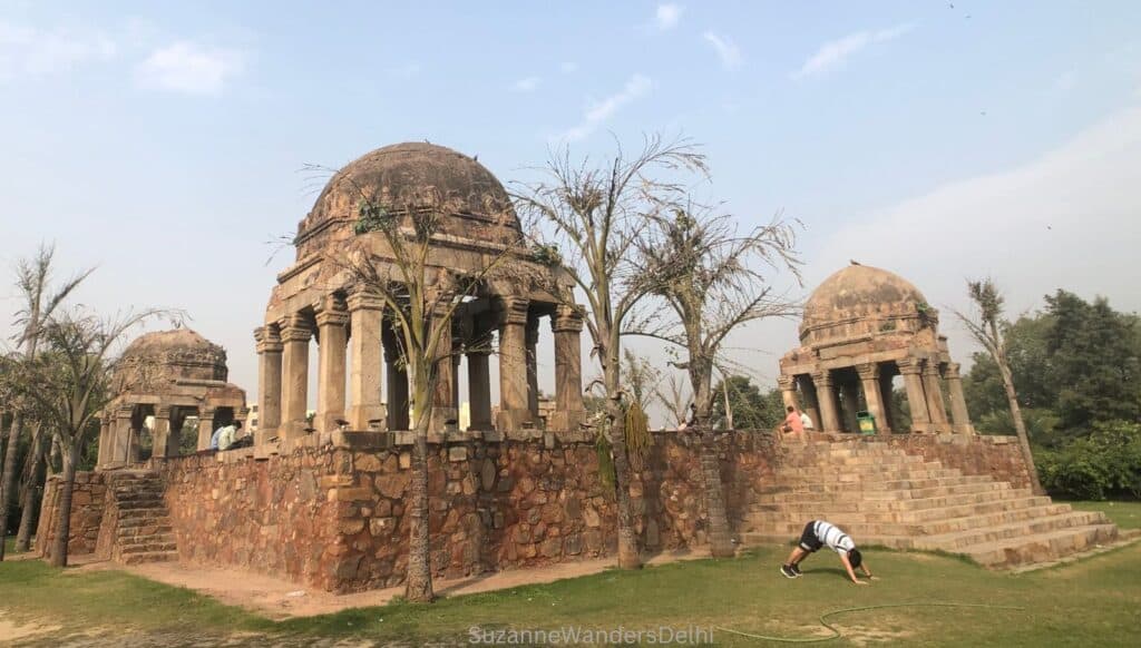 The tomb complex of Darya Khan, e pavilions on a raised platform and a man doing yoga in front on the lawn.