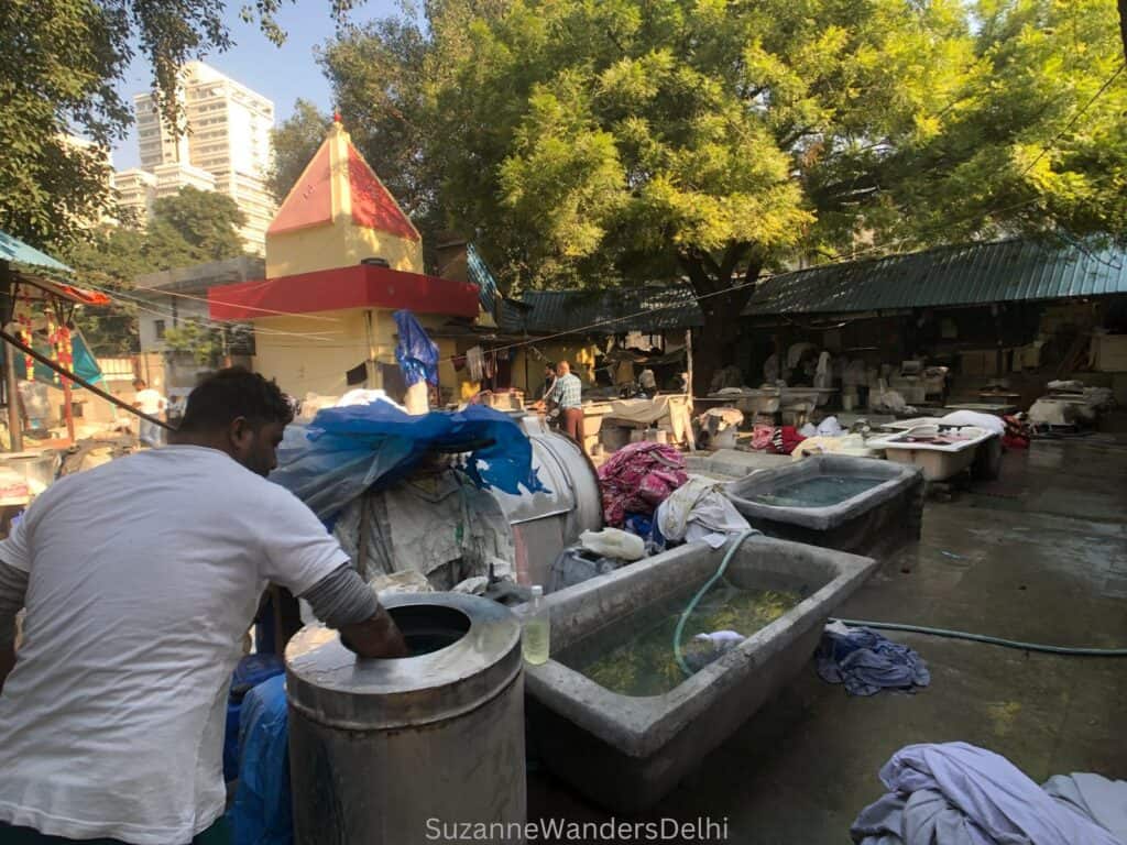 A man washing clothes by hand and big tubs of water at the dhobi ghat in Delhi
