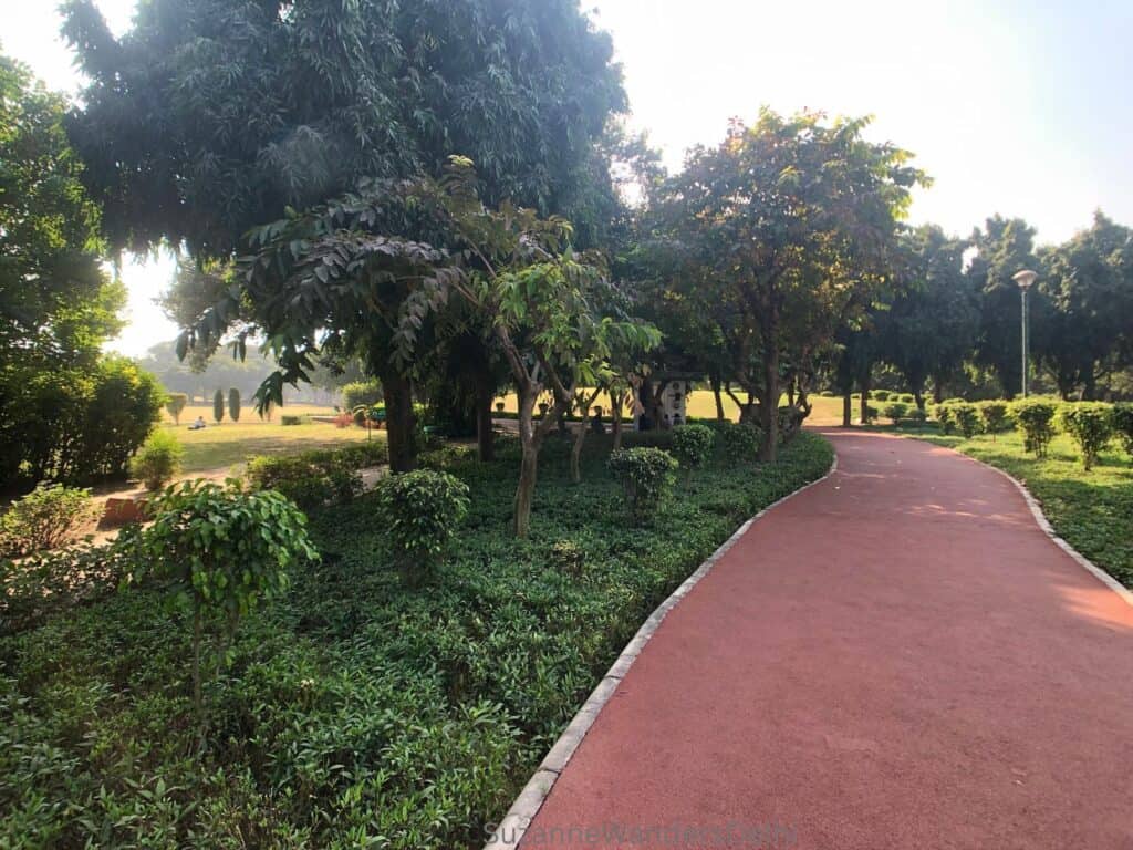 A red paved path surrounded by trees and shrubbery in Nehru Park, Delhi