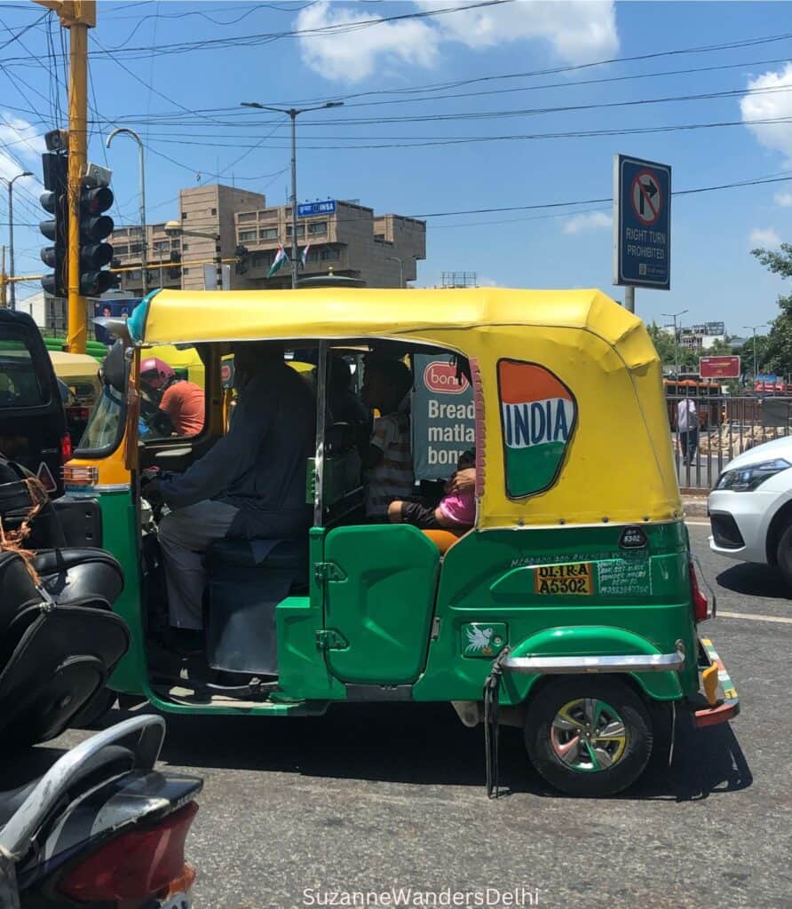 A Delhi auto rickshaw on a busy street with a bright blue sky