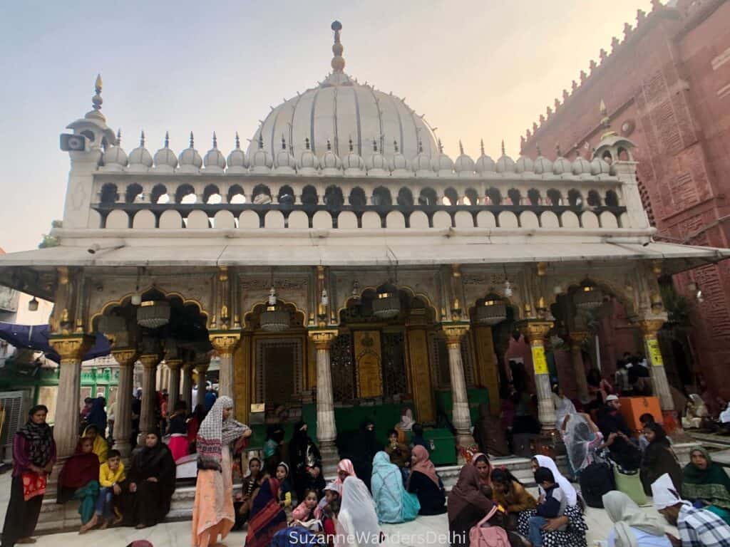 Exterior view of the durgah with female pilgrims sitting outside of it at Hazrat Nizamuddin Dargah, one of the most fascinating off the beaten path sites in Delhi