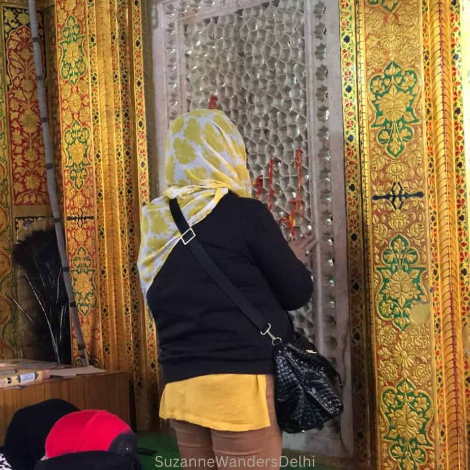 women in yellow scarf tying threads onto the jali of the golden painted tomb
