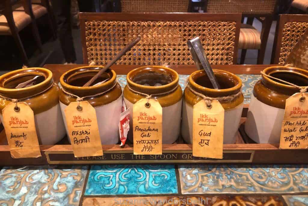 A tray of 5 clay jars with tags on a tiled table