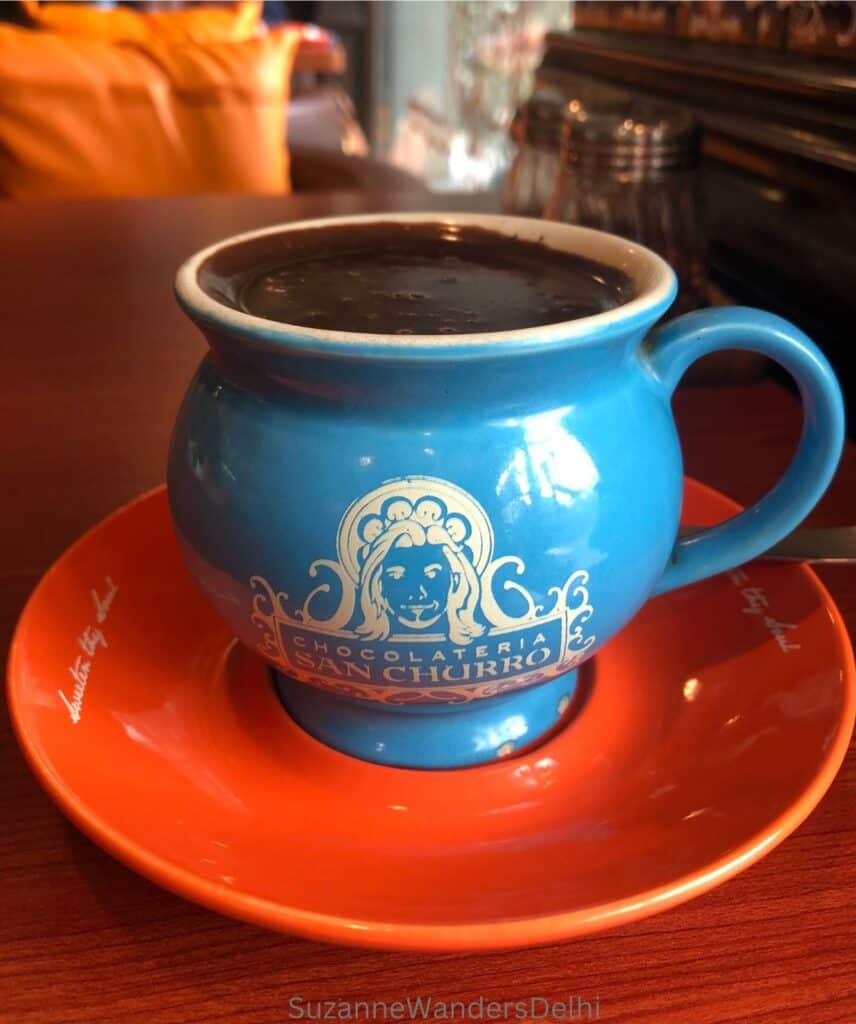 A colourful blue cup with restaurant logo on an orange place at Chocolateria San Churro, one of the very best hot chocolates in Delhi