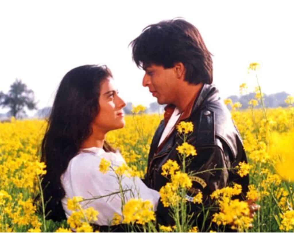 A scene from the movie DDLJ, Shah Rukh Khan and Kajol staring lovingly at each other in a flowering mustard field