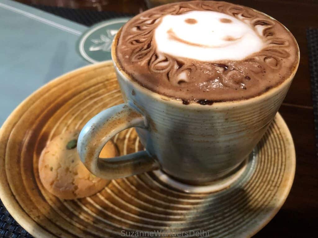 cup of hot chocolate with a milky smiley face on a saucer with a cookie.