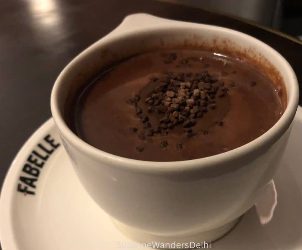 white cup of hot chocolate with chocolate nibs on top on a Fabelle saucer, one of the best hot chocolates in Delhi