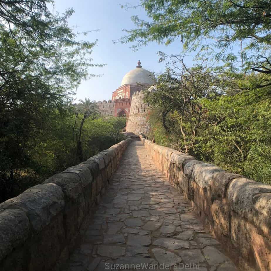 Stone foot bridge and fortified tomb with trees, at Tughlaqabad Fort, one of the most underrated things to do in Delhi