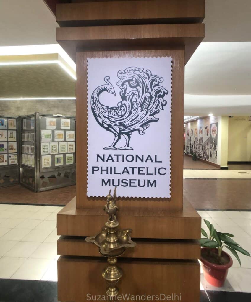 Large wooden column with National Philatelic Museum signage shaped like a stamp featuring a peacock