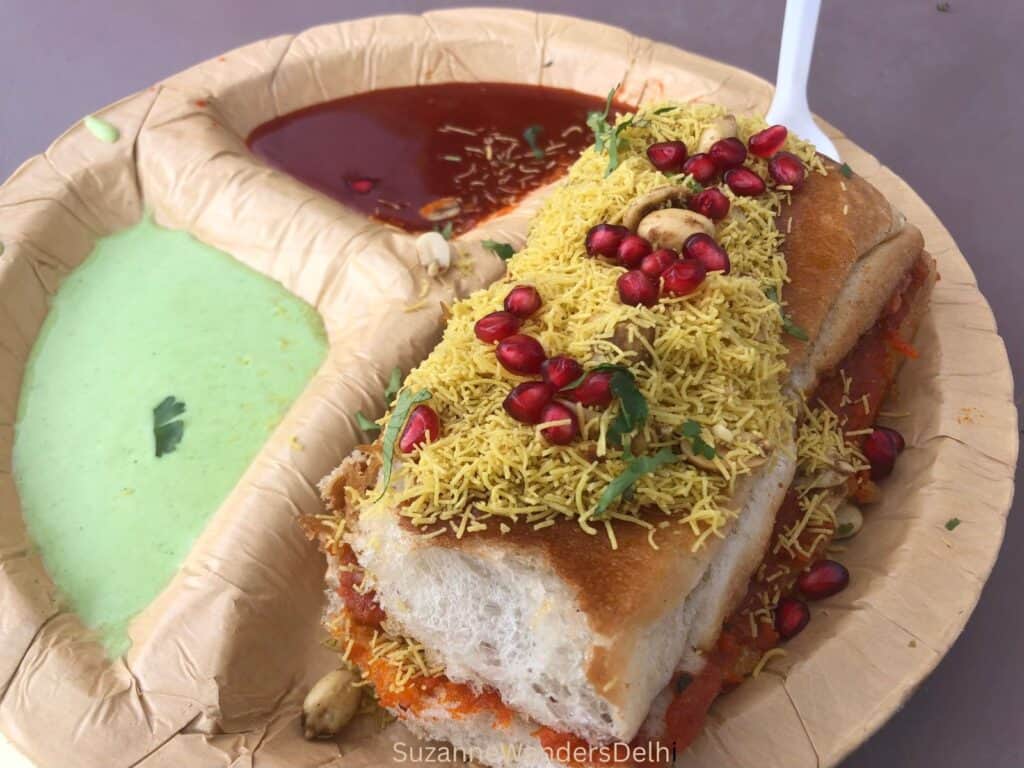 Plate of bombay kachchi dablei smothered in pomegranate seeds and peanuts with tamarind and green chutneys on the side