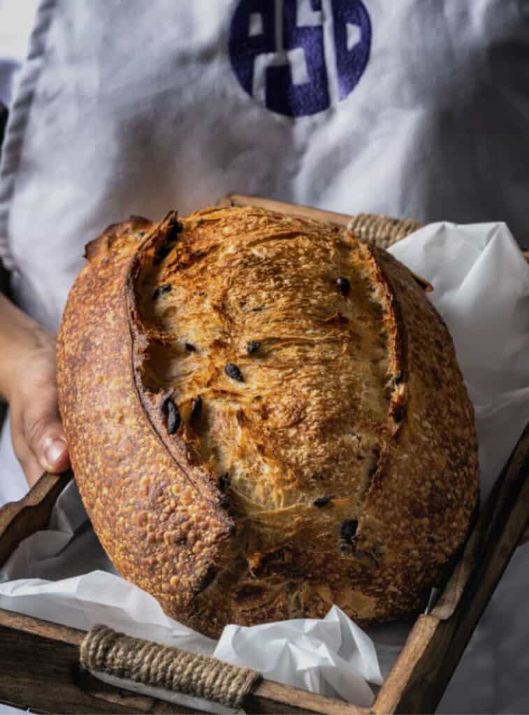 A loaf of sourdough from Project Sweet Dish, with the chef in the background
