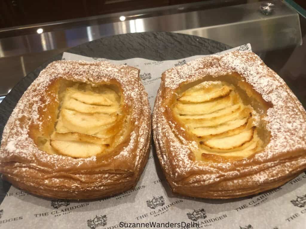 two apple danish side by side on white Claridges paper, dusted in icing sugar
