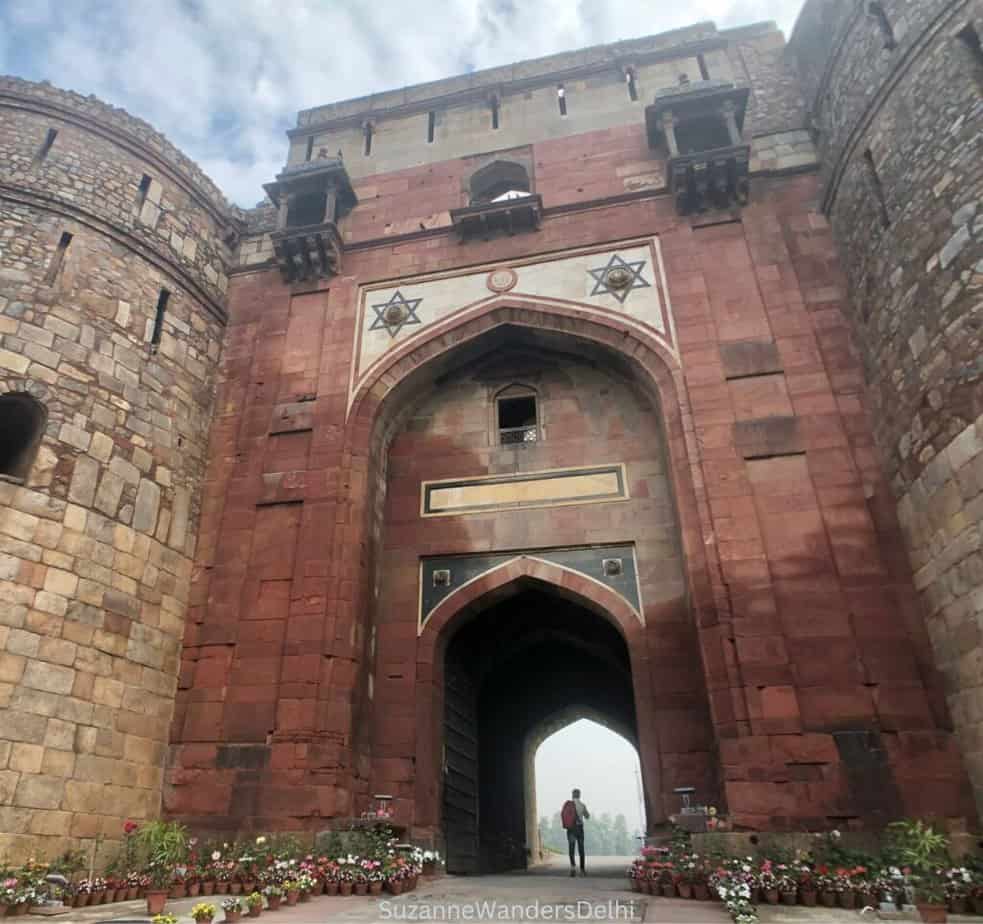 View of Bara Darwaza at Pura Qila with man standing in archway and blue sky overhead, one of the reasons Delhi is worth visiting