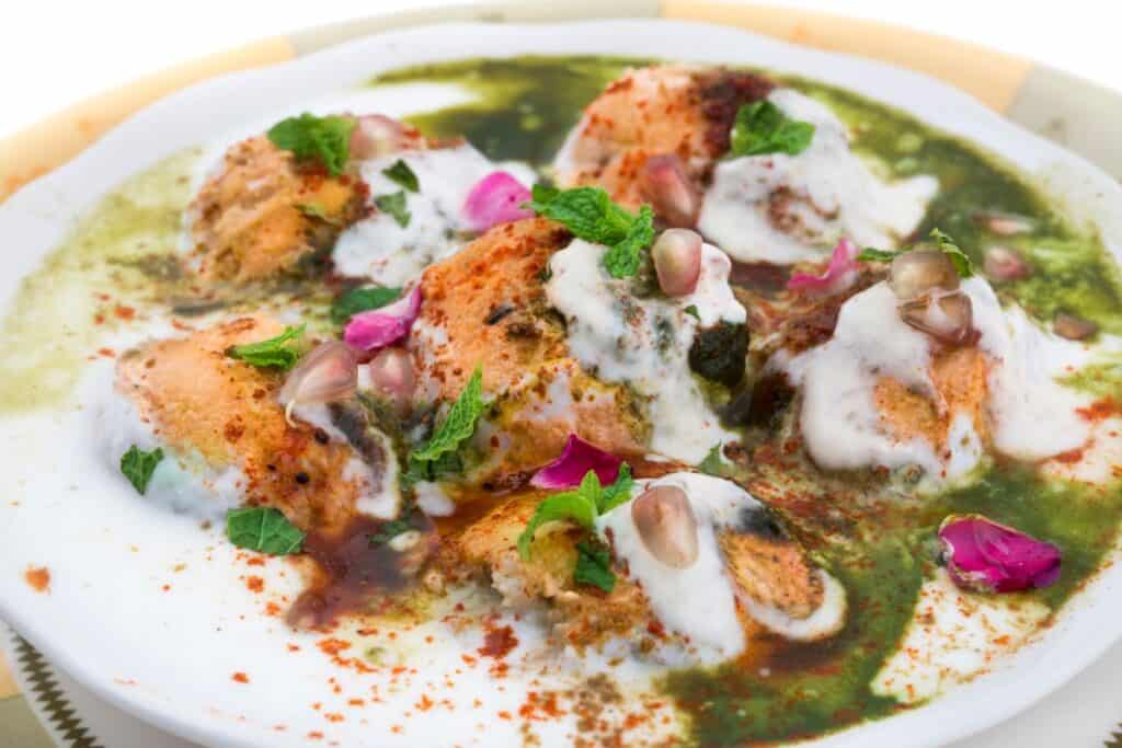 A plate of dahi bhalla smothered in green chutney and yogurt, one of the most refreshing summer Delhi street foods