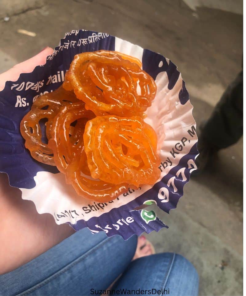 A plate of five orange jalebis on a blue and white paper plate