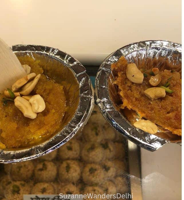 two little aluminum bowls of hava side by side on a glass display counter with Indian sweets below at Shyam Sweets in Old Delhi, one of the best places on a street food tour