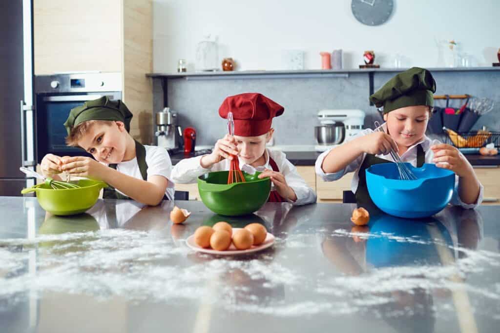 3 children side by side cracking eggs and whipping something in bowls in a kitchen cooking class, one of the best things to do with kids in Delhi