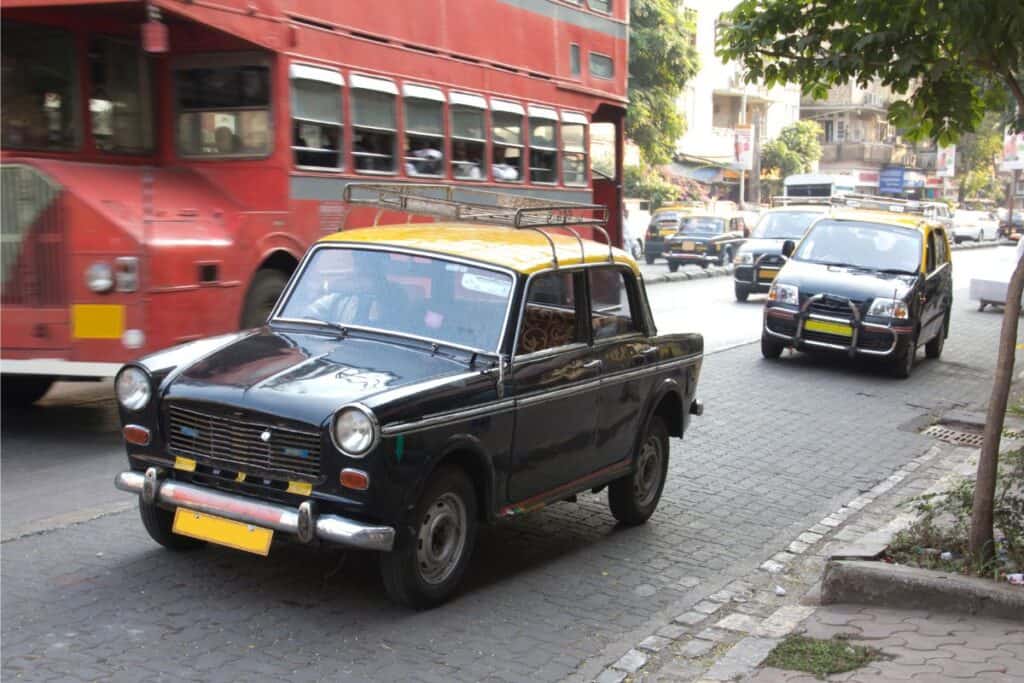 a Mumbai taxi with old double decker red bus in background on Mumbai street