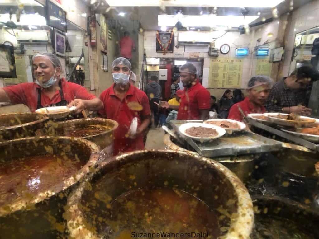 Big pots of dal and 4 cooks behind a dal plashed front window of Kaka di Hotel in Delhi