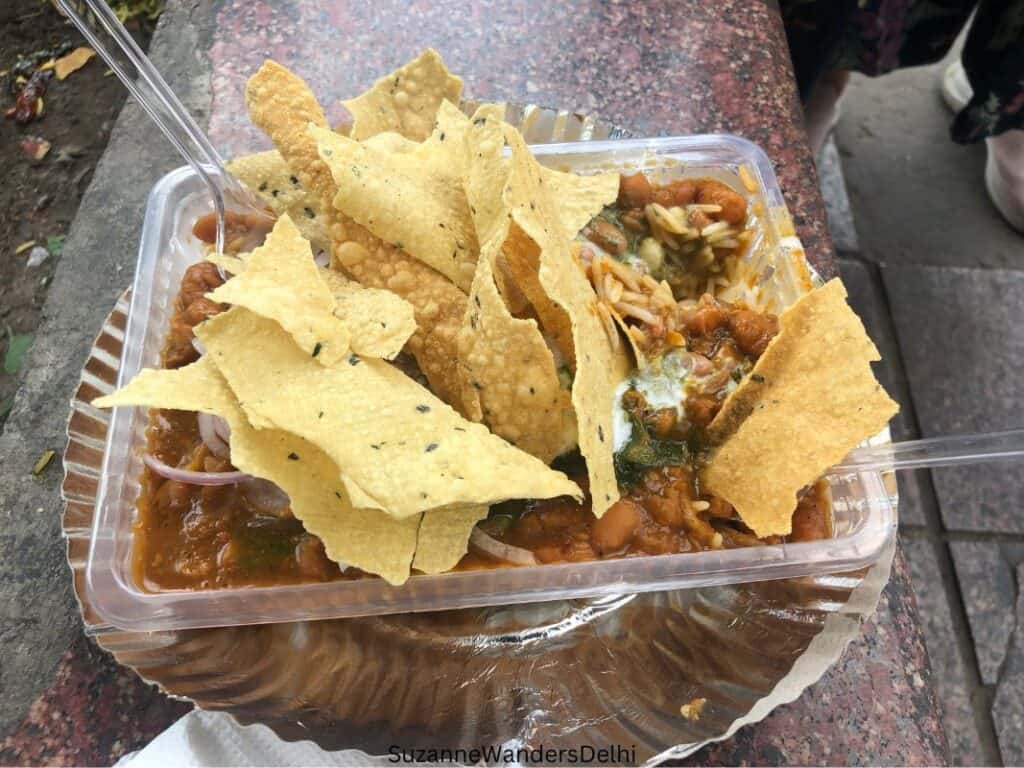 A plastic dish of rajma chawal with broken papad on top outside of Parashar Foods in Connaught Place, one of 3 markets for street food that aren't in Old Delhi