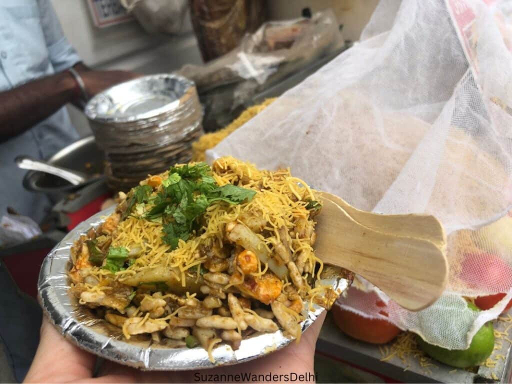 A plate of bhel puri with the bhel puri stand in the background