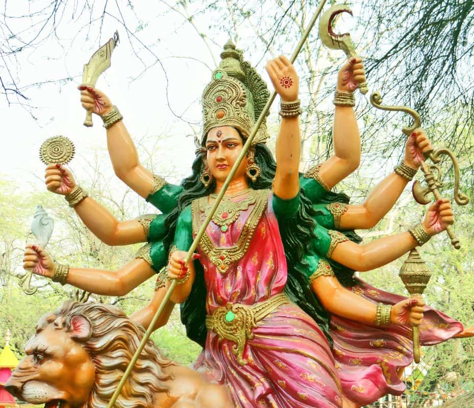The goddess Durga with her 10 arms and weapons riding a lion, outside in a treed area