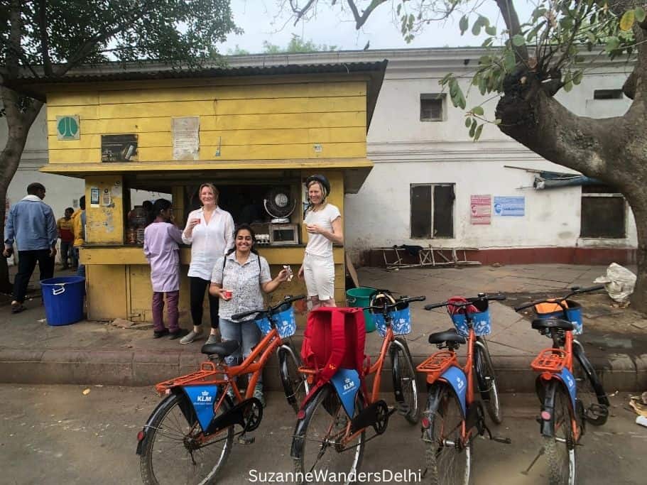 group standing around drinking chai in front of parked bikes on Delhi By Cycle tour