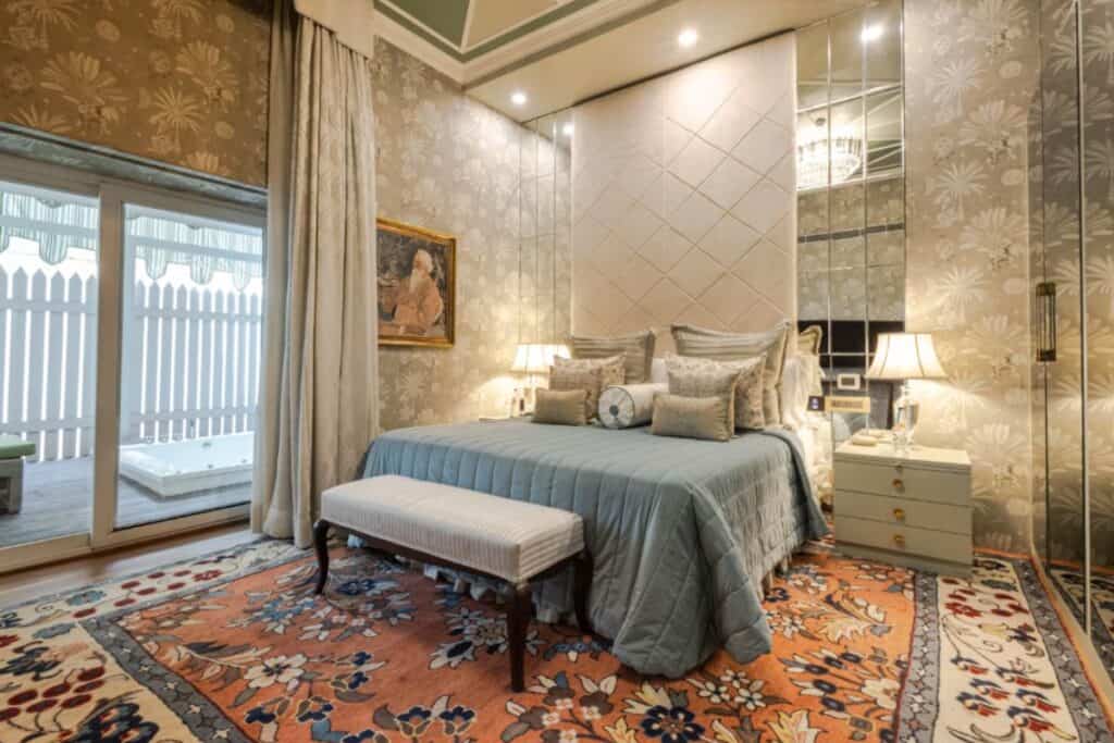 King size bed with grey bedding and many decorative pillows in cream and gold decorated room with Persian rug at the Claridges Hotel New Delhi