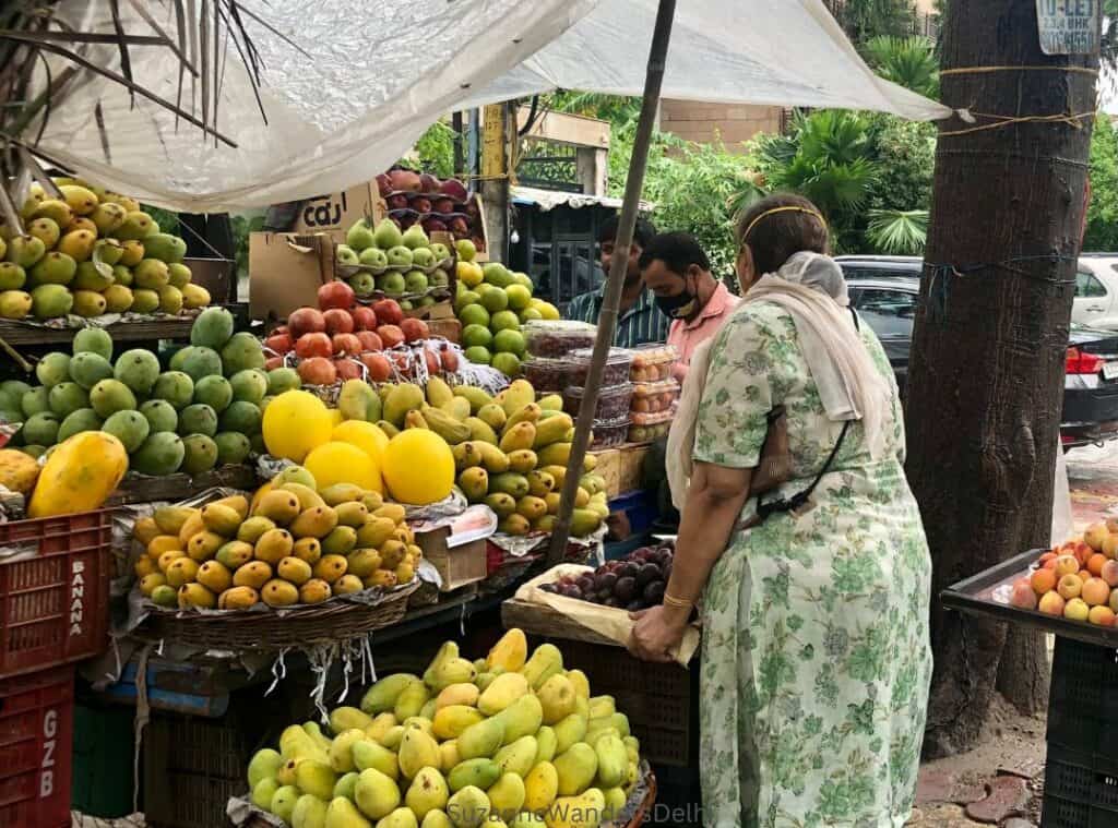 a fruit stand with stack of mangoes and an Indian woman shopping