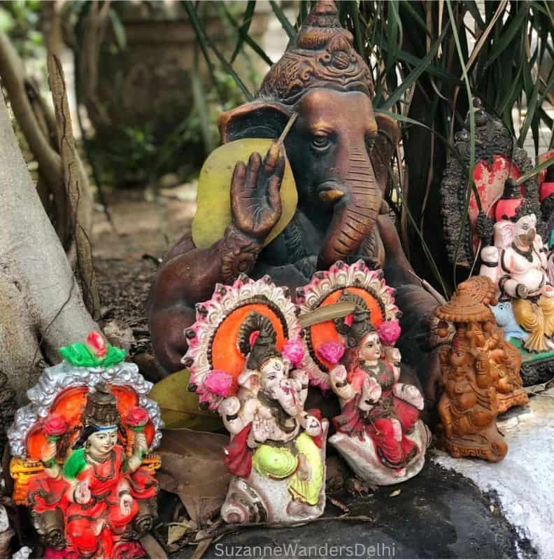 5 small religious statues with a larger wooden Lord Ganesha behind at the base of a tree in Delhi, religion is major part of the culture of Delhi