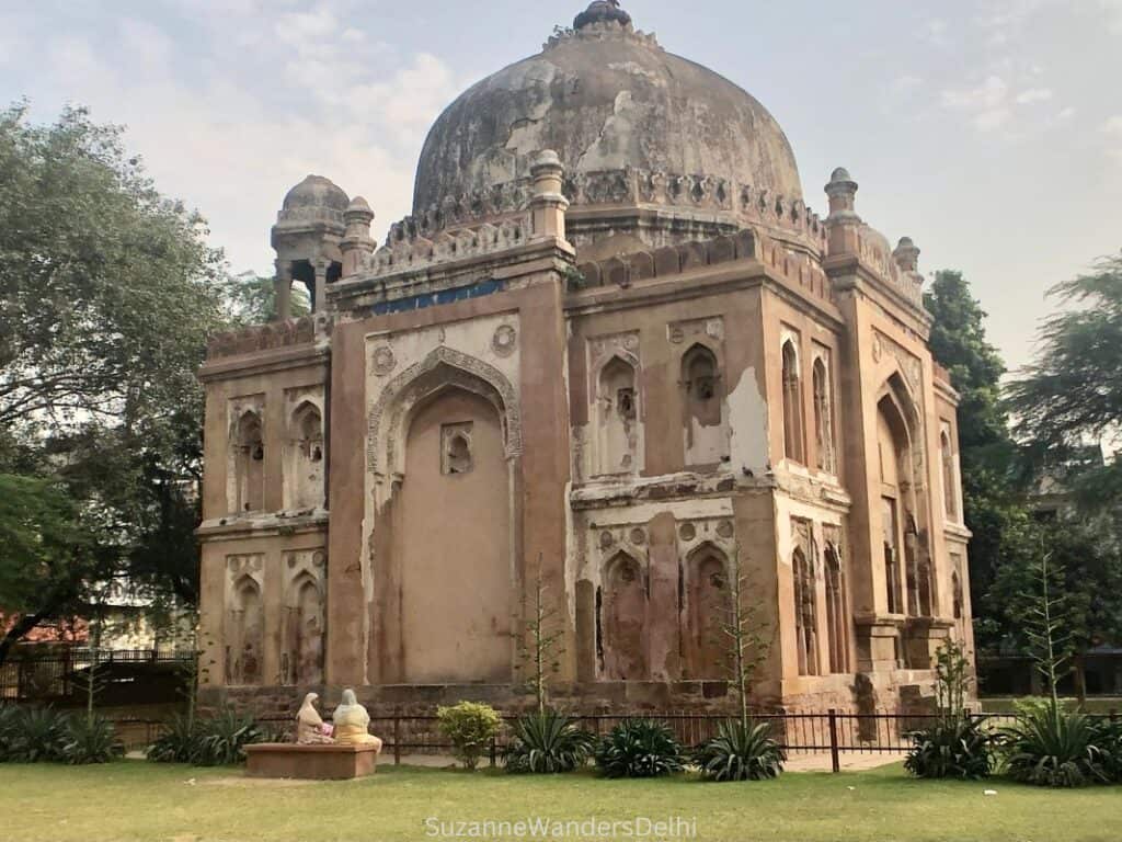 Side full view of one of the Warzipur tombs with two Indian women sitting on a bench in front of it