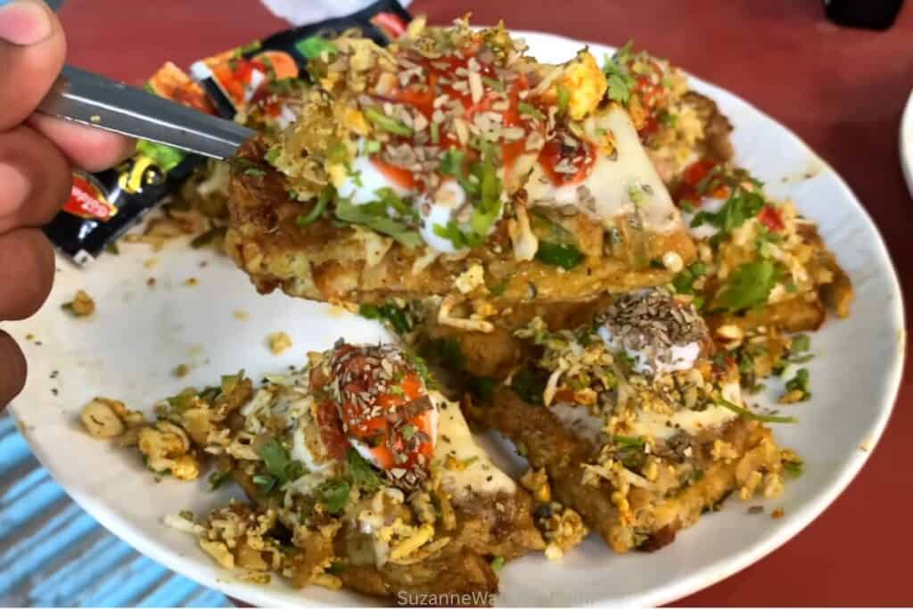 A white plate with loaded omelette topped with masala, cheese, cilantro and chopped onion