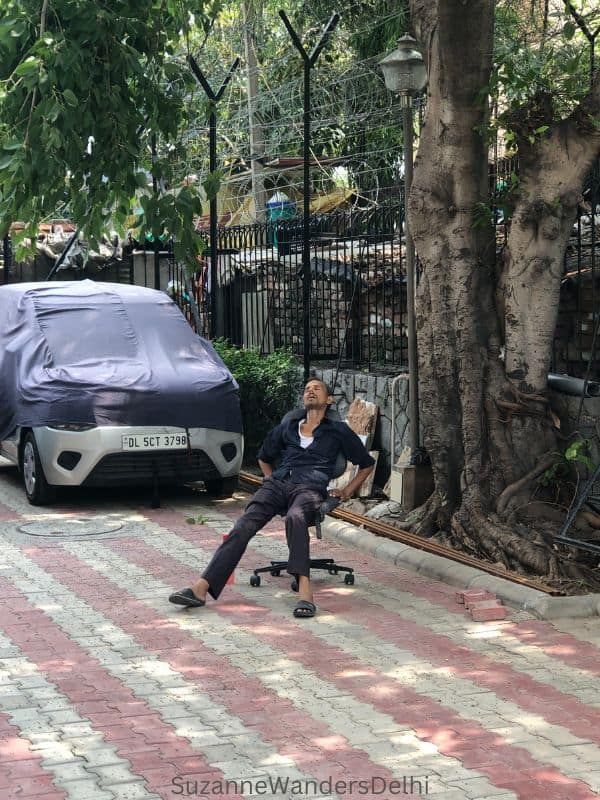 man fast asleep in a chair in a driveway with a car behind him - must be one of the most off the beaten path sites in Delhi