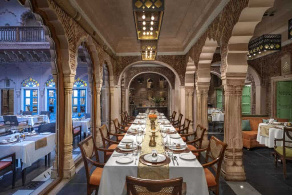 The indoor fine dining room at Lakhori, a long view of a laid table with arched pillars on both sides - one of Delhi's most famous restaurants