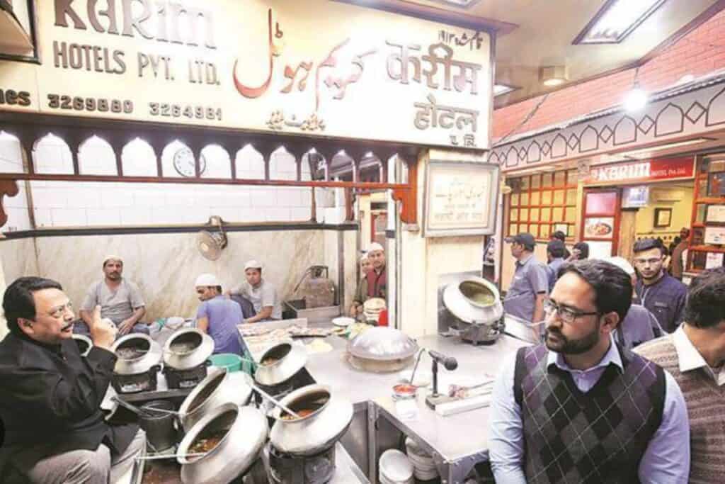 server sitting in front of metal cauldrons of food at Karim's in Old Delhi
