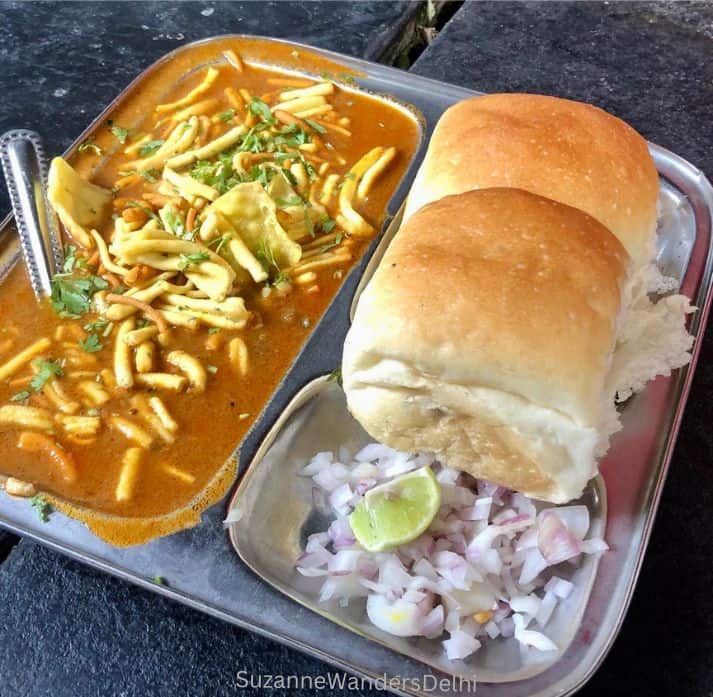 a plate of misal pav with chopped onion and lime garnish, cooked street food is safe for tourists to eat in India