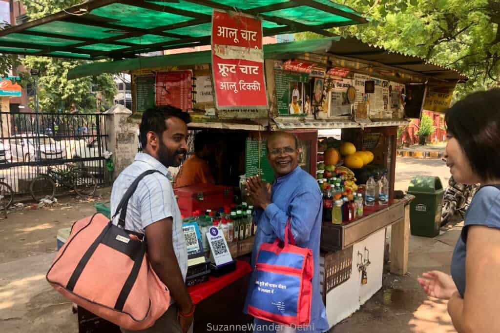 A chaat stand with green awning and two Indian men in front on a leafy street in Delhi