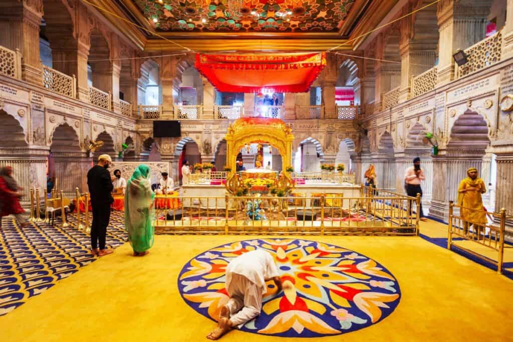 a man kneeling down and praying facing the shrine inside Gurudwara Sis Ganj Sahib 