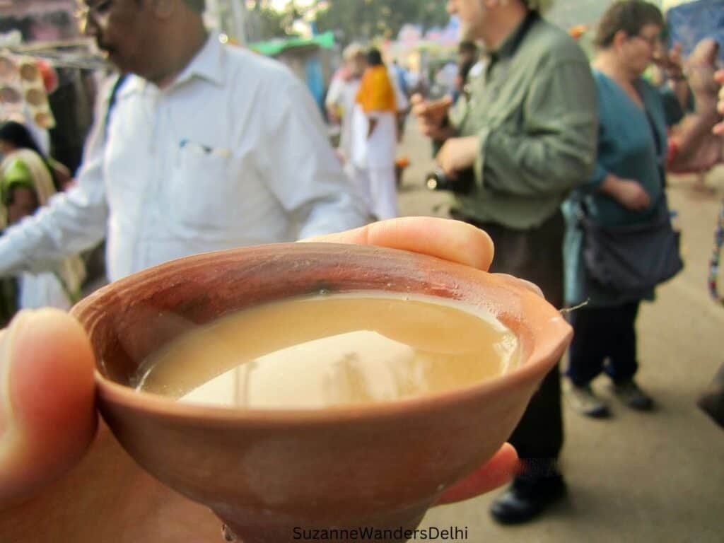 clay cup of chai being held by hand with people in background, chai is safe for tourists to drink in India