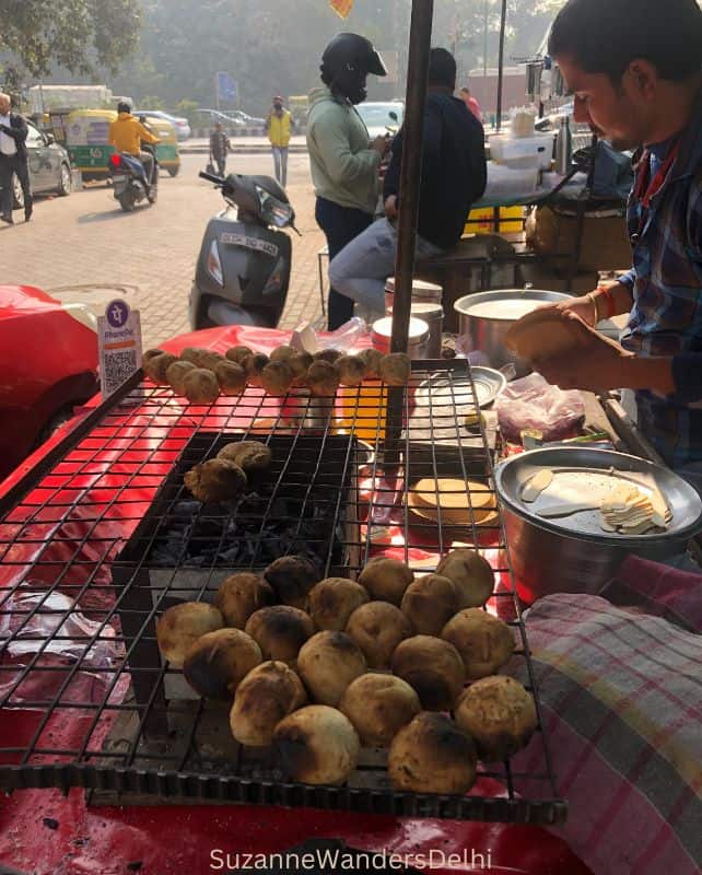 A wala cooking lentil balls over a charcoal burner on a table top in a market, this is safe for tourists to eat in India