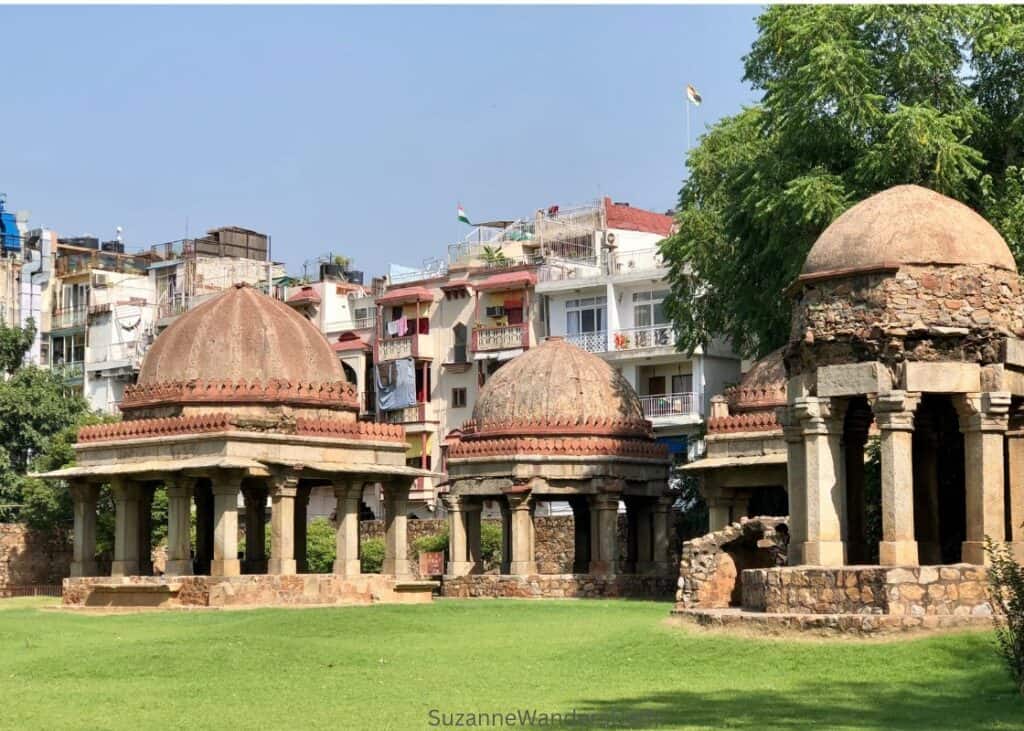 view of 3 domed pavillions on grassy lawn with white residential buildings behind in Hauz Khas Complex, Delhi