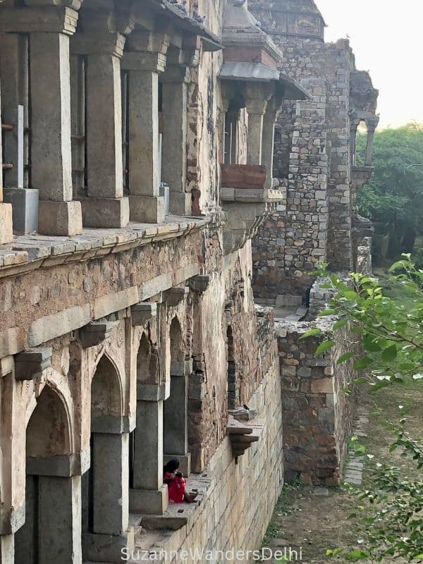 side view of ancient madrasa in Hauz Khas Comlex, Delhi with girl sitting in arched open window wearing red